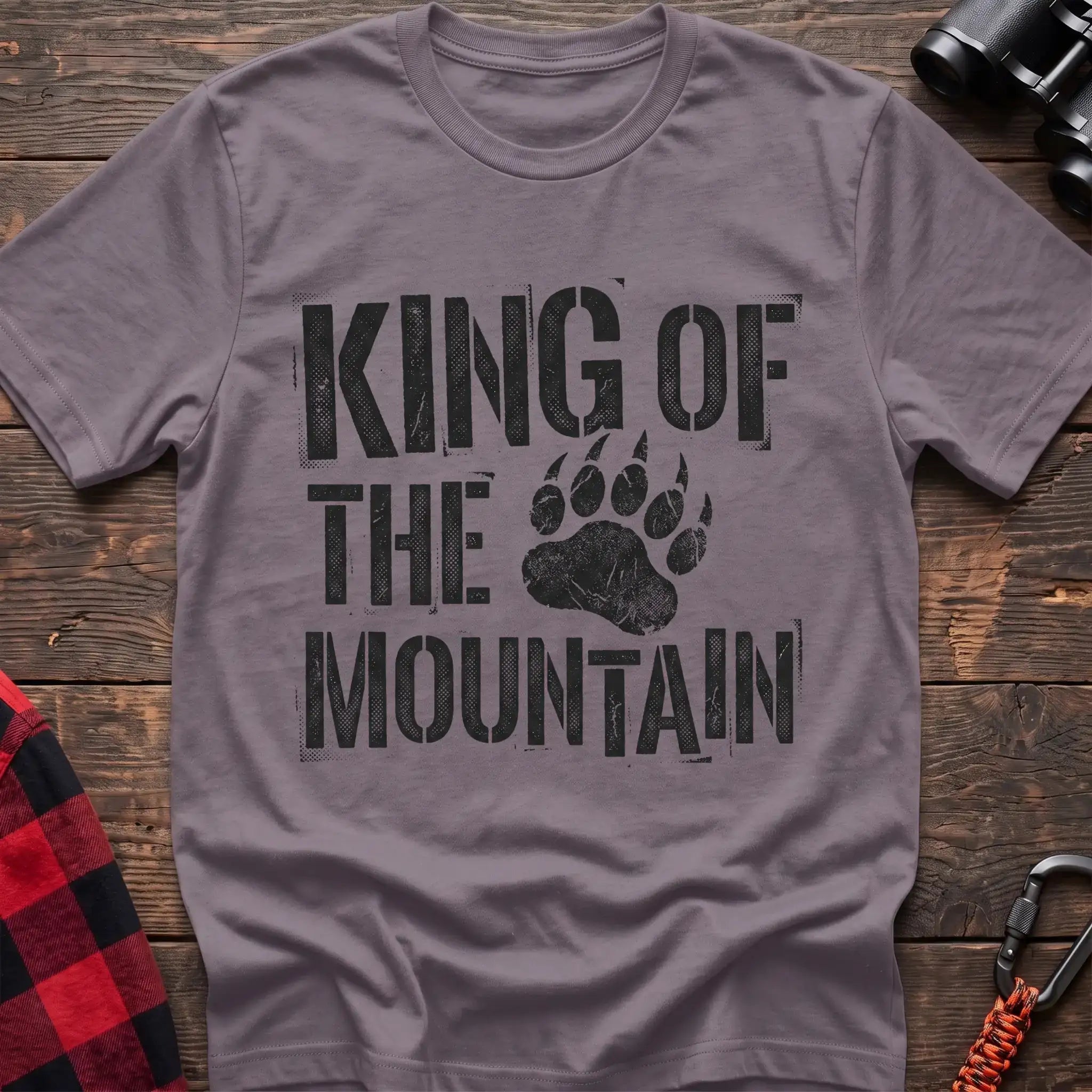 Paragon t-shirt with distressed black text reading “KING OF THE MOUNTAIN” and a large bear paw print integrated into the design, laid flat on a wooden surface.