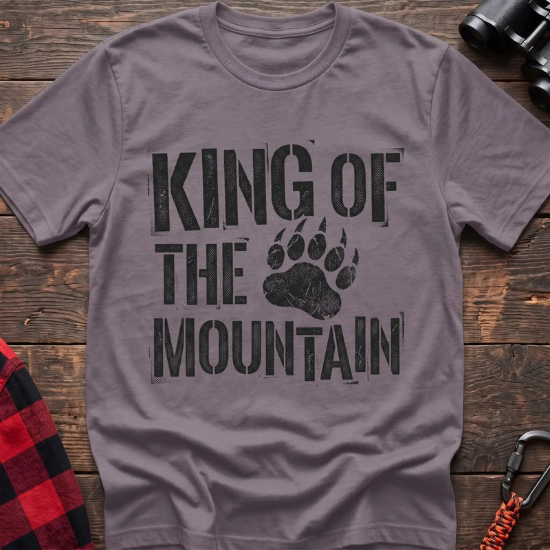 Paragon t-shirt with distressed black text reading “KING OF THE MOUNTAIN” and a large bear paw print integrated into the design, laid flat on a wooden surface.