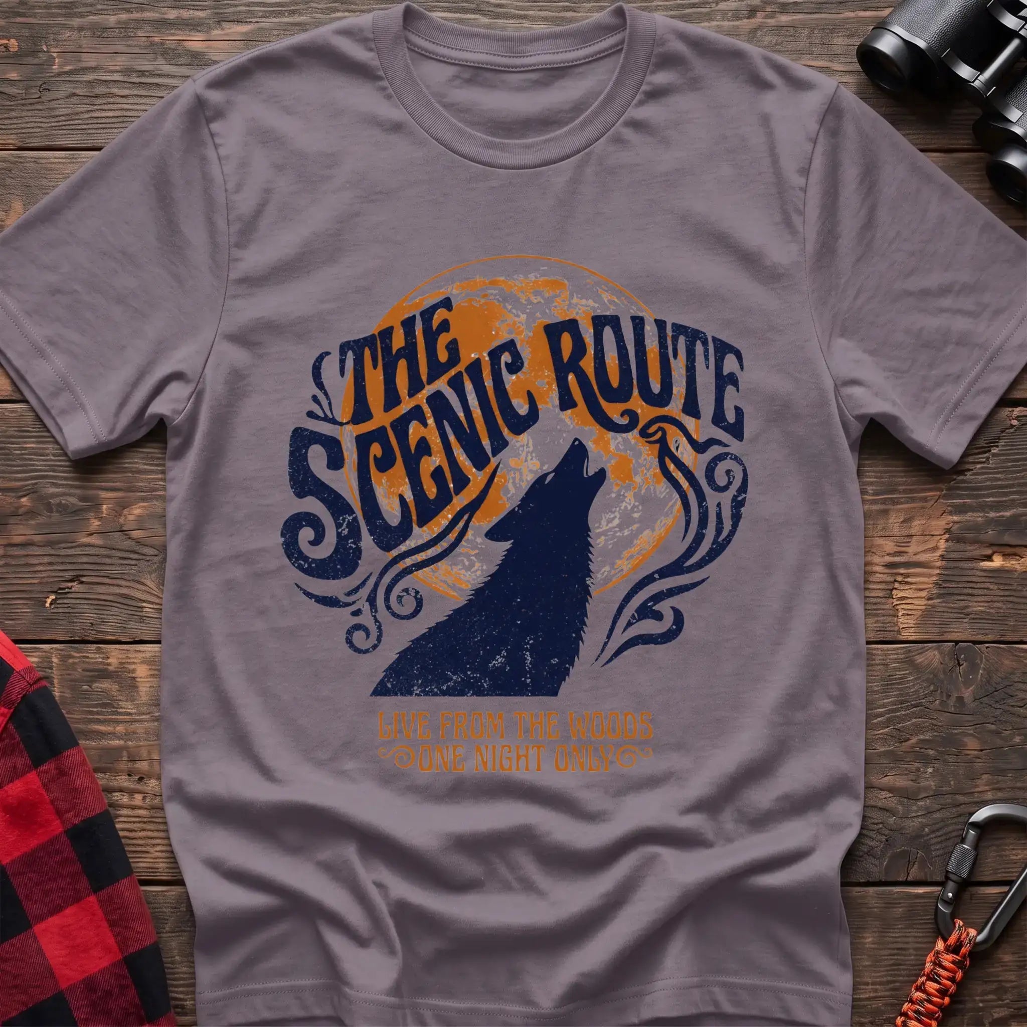 Paragon t-shirt with a dark blue howling wolf silhouette against an orange circle, with the arched text “THE SCENIC ROUTE” above and “LIVE FROM THE WOODS / ONE NIGHT ONLY” below, laid flat on a wooden surface.