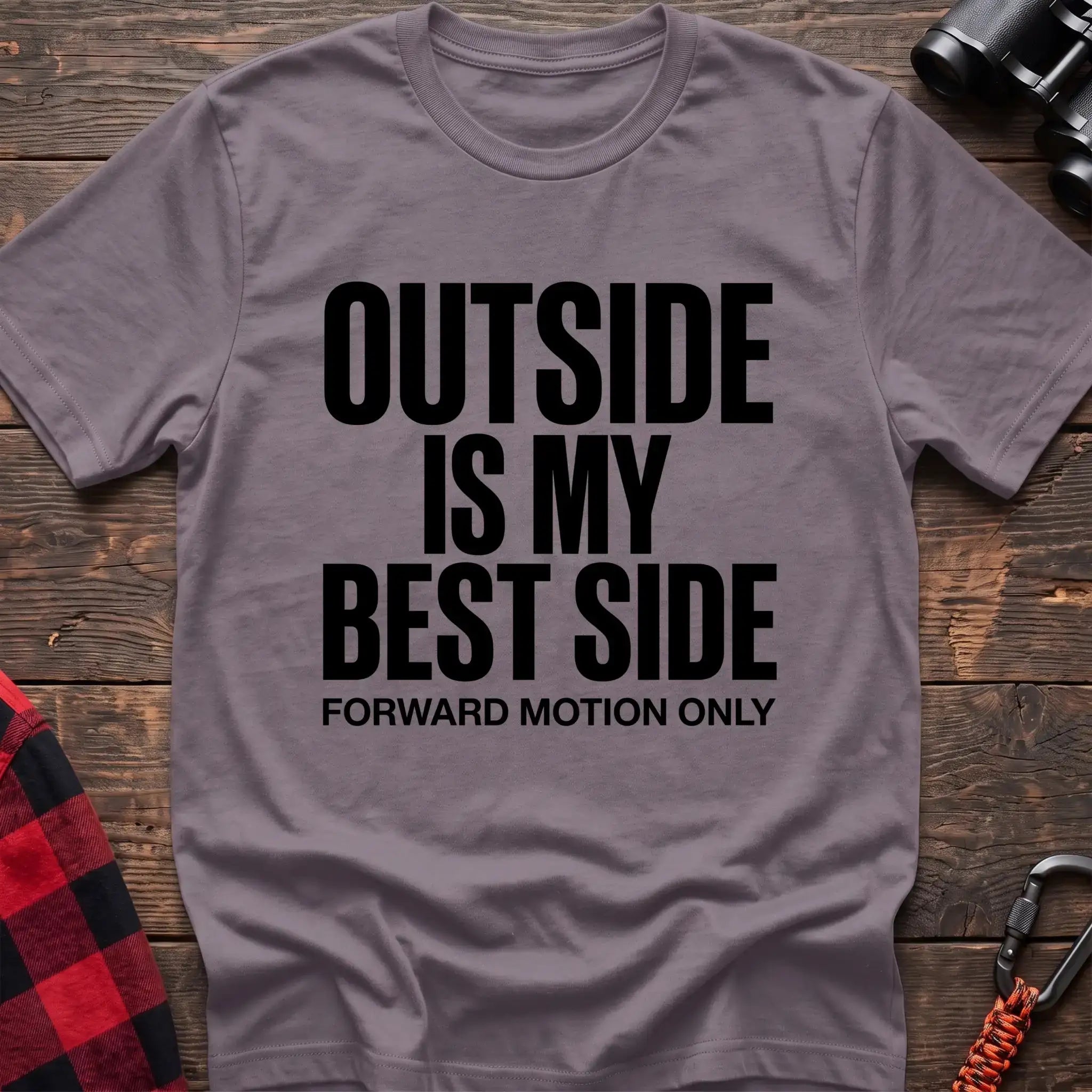 Paragon t-shirt with bold black text reading “OUTSIDE IS MY BEST SIDE” and “FORWARD MOTION ONLY” below it, laid flat on a wooden surface.