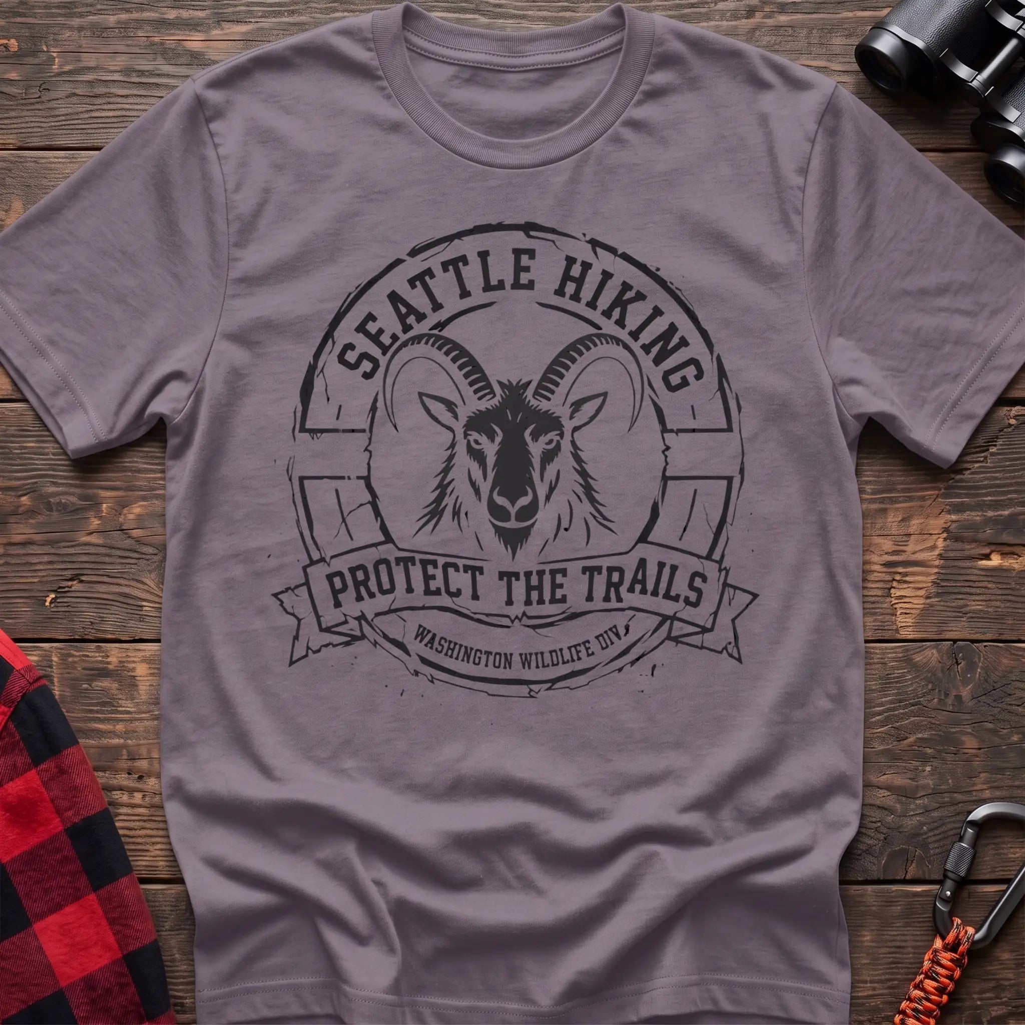 Paragon cotton t-shirt with vintage Seattle Hiking graphic of a mountain goat in a circular badge, Protect the Trails Washington Wildlife Division design, flat lay on rustic wood with hiking gear