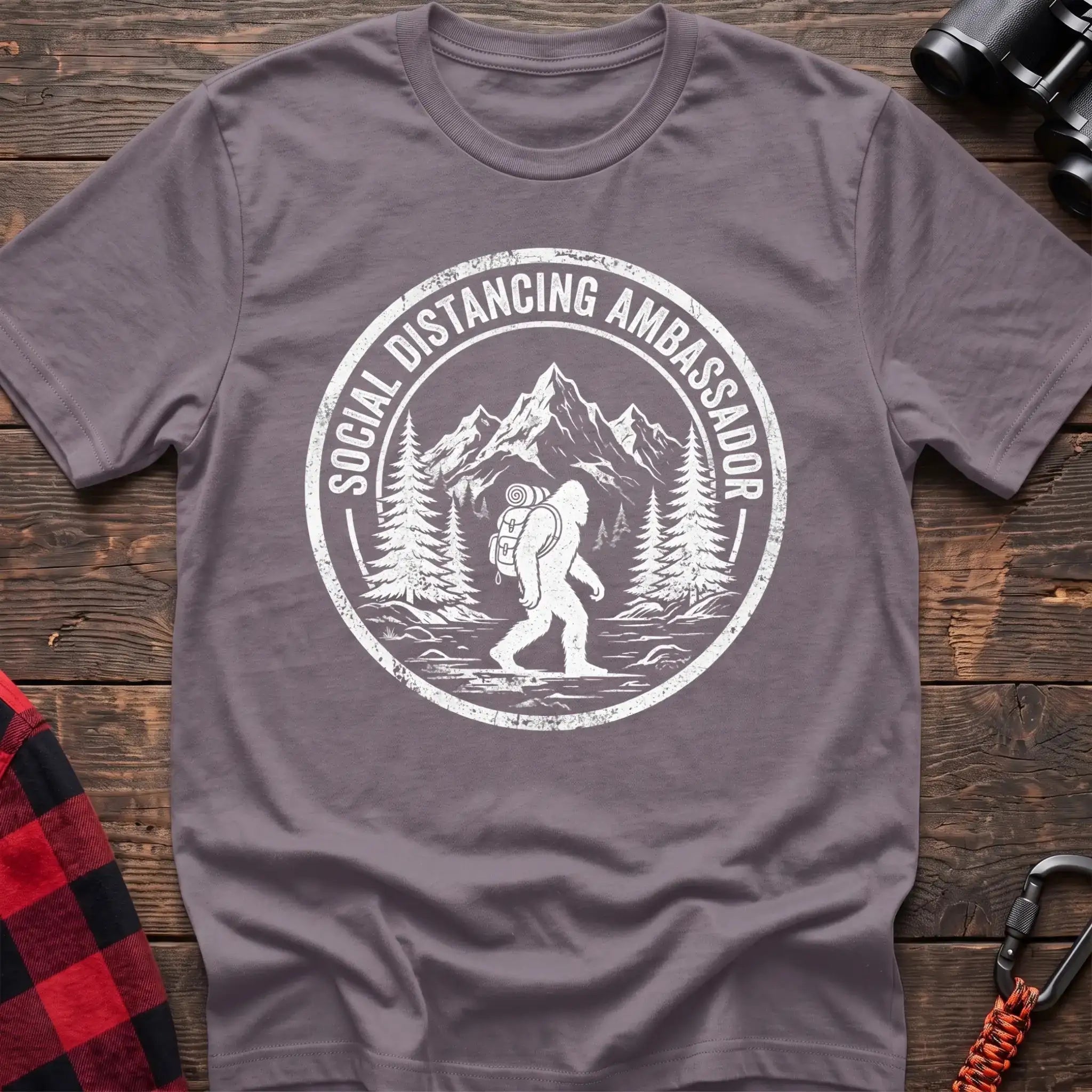 Paragon t-shirt with white circular badge graphic of Bigfoot hiking with a backpack through mountains and the text Social Distancing Ambassador