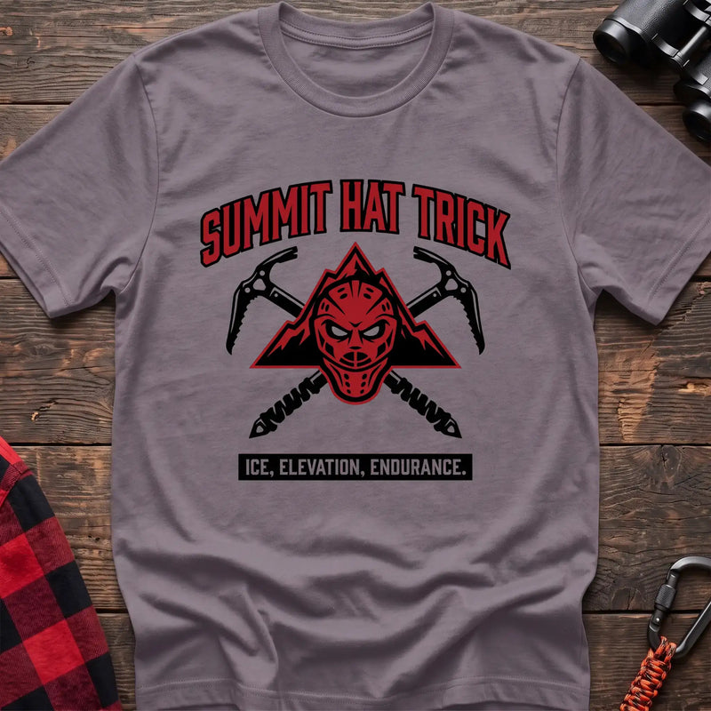 Paragon t-shirt with a red mountain-themed goalie mask and crossed ice axes, with the text “SUMMIT HAT TRICK” and “ICE, ELEVATION, ENDURANCE,” laid flat on a wooden surface.