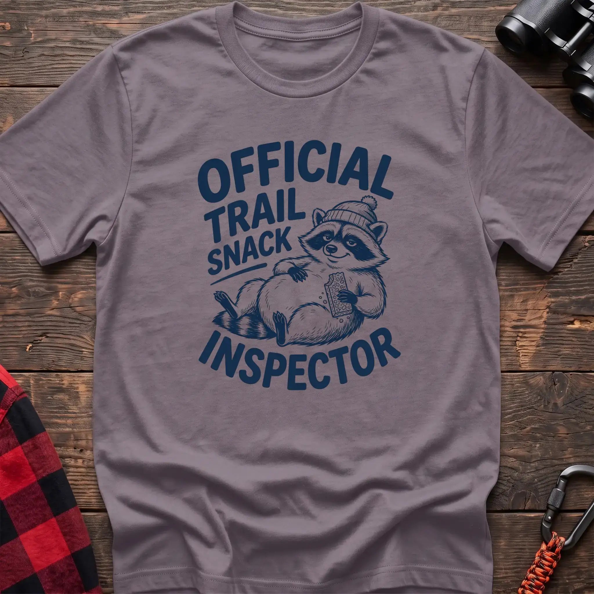 Paragon t-shirt with cartoon raccoon holding a snack and the text Official Trail Snack Inspector
