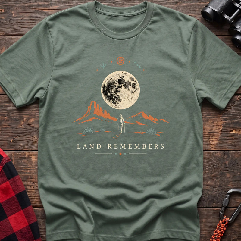 Sage cotton t-shirt with a desert hiker and full moon graphic and Land Remembers text on rustic wood