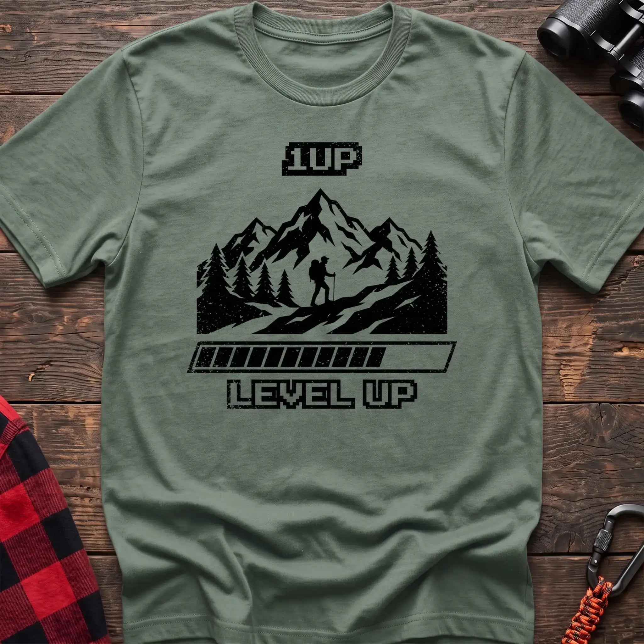 Sage t-shirt with black graphic of a hiker on a mountain trail under pixel-style 1UP text and a progress bar reading Level Up