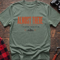 Sage cotton t-shirt with a mountain graphic and Almost There Everyone Ahead of Me text on rustic wood