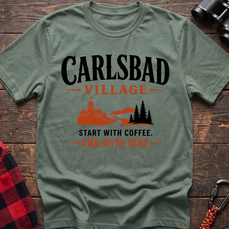 Sage cotton t-shirt with a village and trail graphic and Carlsbad Village Start with Coffee End with Dirt text on rustic wood