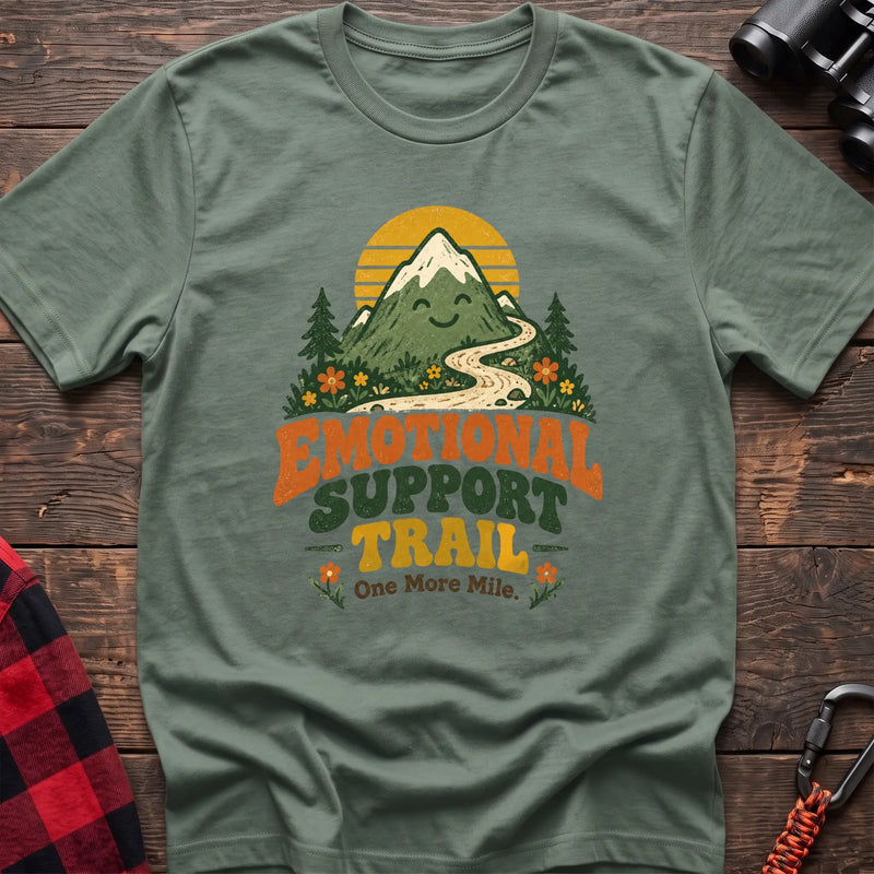 Sage cotton t-shirt with a smiling mountain and trail graphic and Emotional Support Trail text on rustic wood