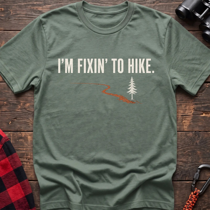 Sage cotton t-shirt with a trail and pine graphic and I’m Fixin’ to Hike text on rustic wood