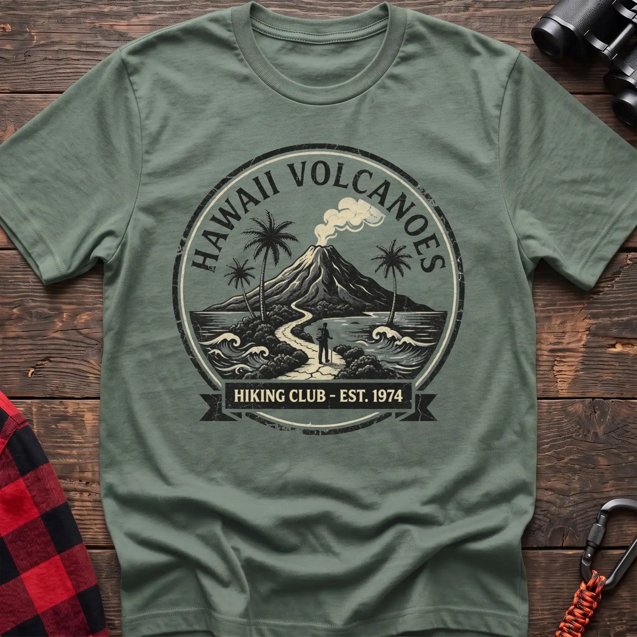 Sage t-shirt with circular Hawaii Volcanoes badge graphic showing a volcano, palm trees, and a hiker, reading Hiking Club Est 1974