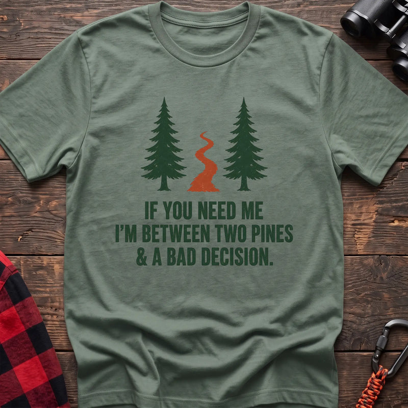 Sage cotton t-shirt with two pines and a trail graphic and If You Need Me I’m Between Two Pines and a Bad Decision text on rustic wood