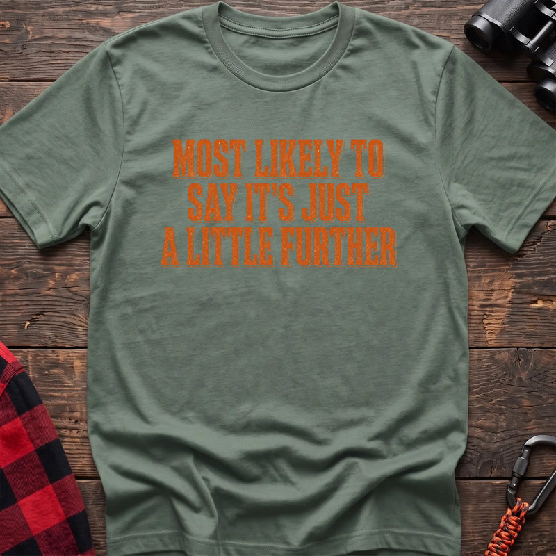 Sage cotton t-shirt with Most Likely to Say It’s Just a Little Further text on rustic wood