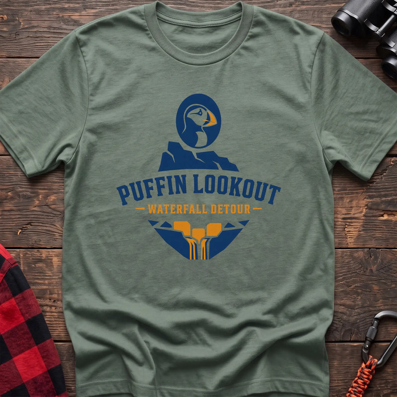 Sage cotton t-shirt with a puffin and waterfall graphic and Puffin Lookout Waterfall Detour text on rustic wood