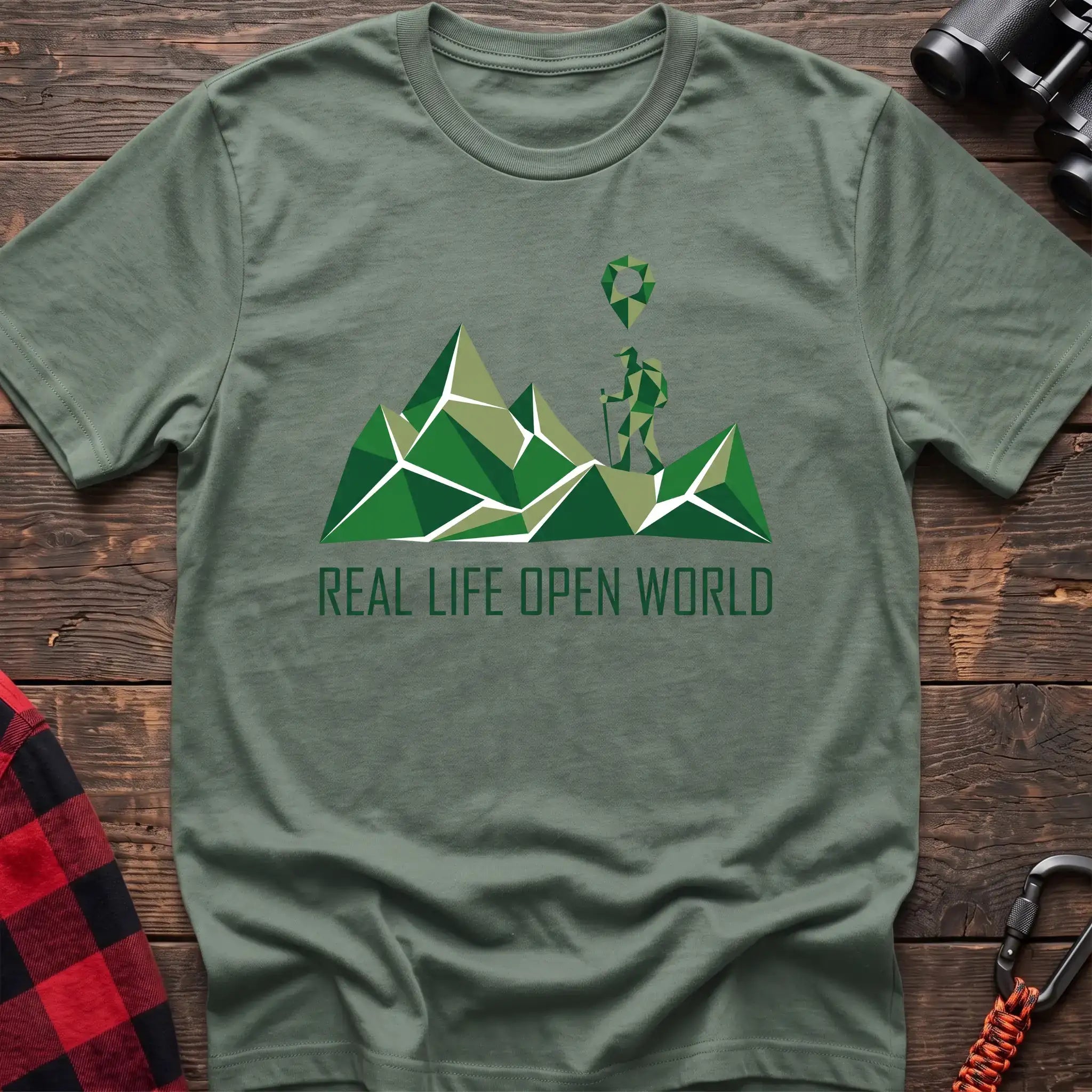 Sage green t-shirt with geometric green mountain graphic and a hiker silhouette under a map pin, reading Real Life Open World