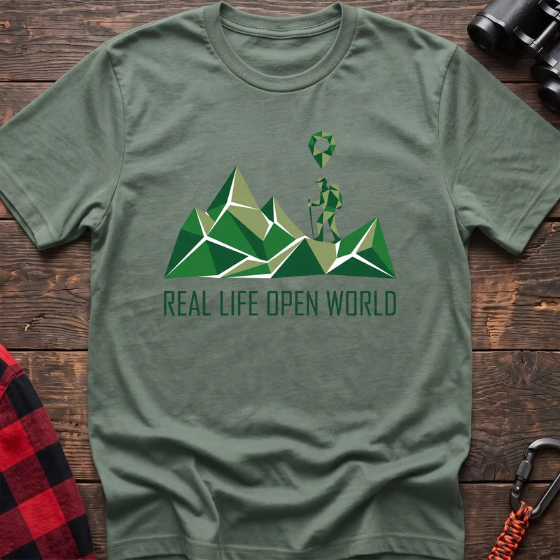 Sage green t-shirt with geometric green mountain graphic and a hiker silhouette under a map pin, reading Real Life Open World