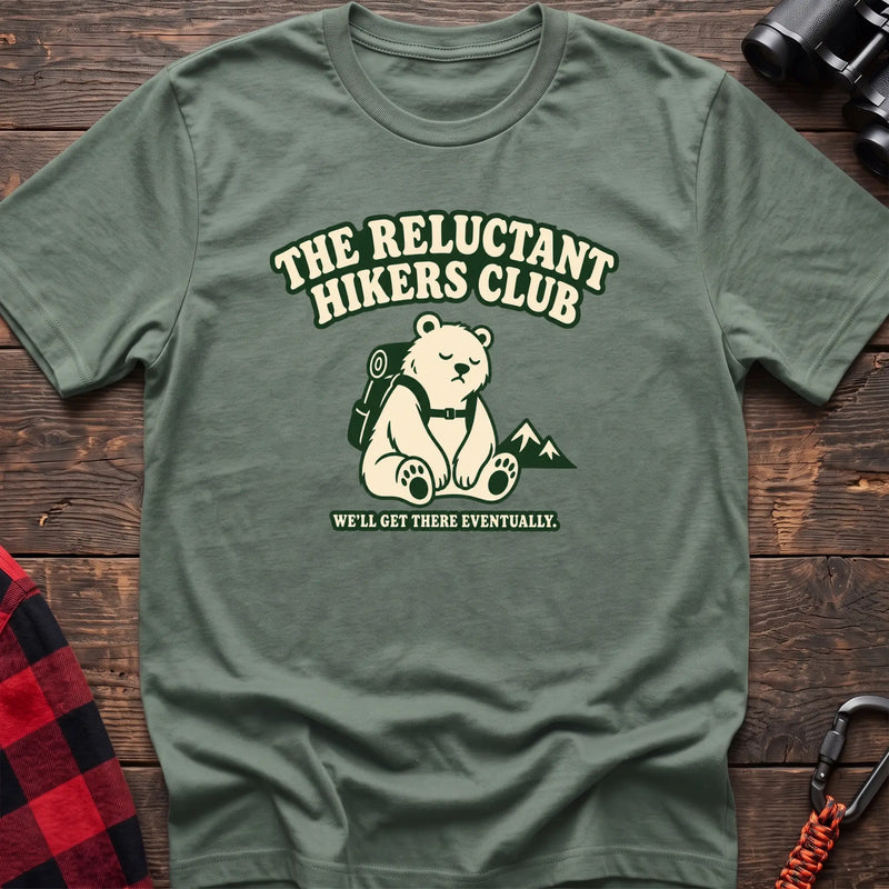 Sage cotton t-shirt with a sitting backpack bear graphic and The Reluctant Hikers Club text on rustic wood