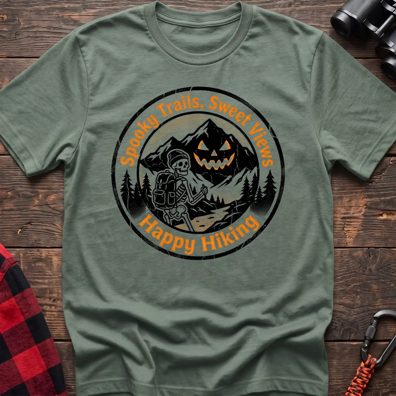 Sage green t-shirt with circular graphic of a skeleton hiker giving a thumbs up in front of a jack-o-lantern mountain, reading Spooky Trails Sweet Views Happy Hiking