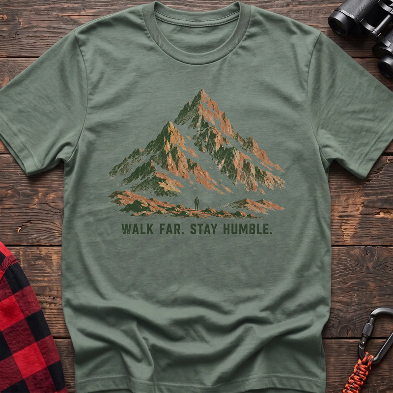 Sage cotton t-shirt with a mountain and hiker graphic and Walk Far Stay Humble text on rustic wood