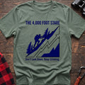Sage t-shirt with a blue illustration of a hiker climbing a steep mountain, with the text “THE 4,000 FOOT STARE” and “Don’t Look Down. Keep Climbing,” laid flat on a wooden surface.