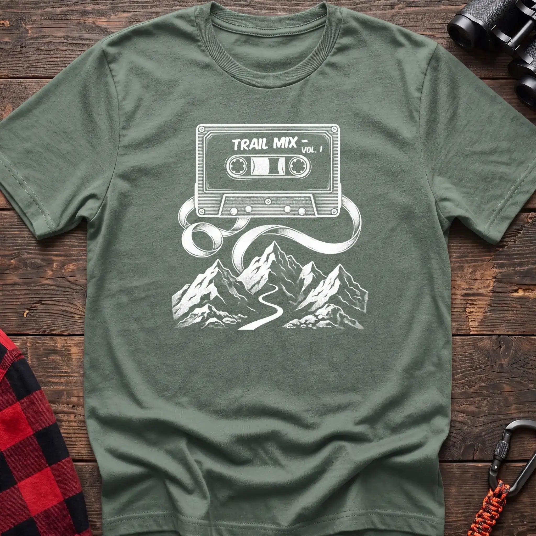 Sage t-shirt with white cassette tape graphic labeled Trail Mix Vol. 1, with tape unspooling into a trail through mountains