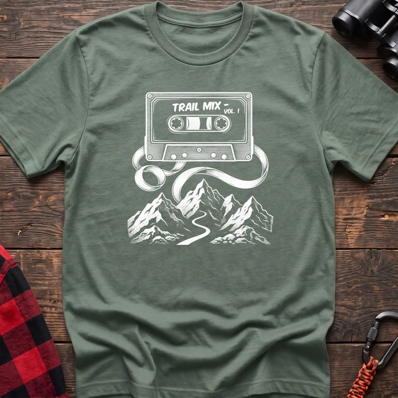 Sage t-shirt with white cassette tape graphic labeled Trail Mix Vol. 1, with tape unspooling into a trail through mountains