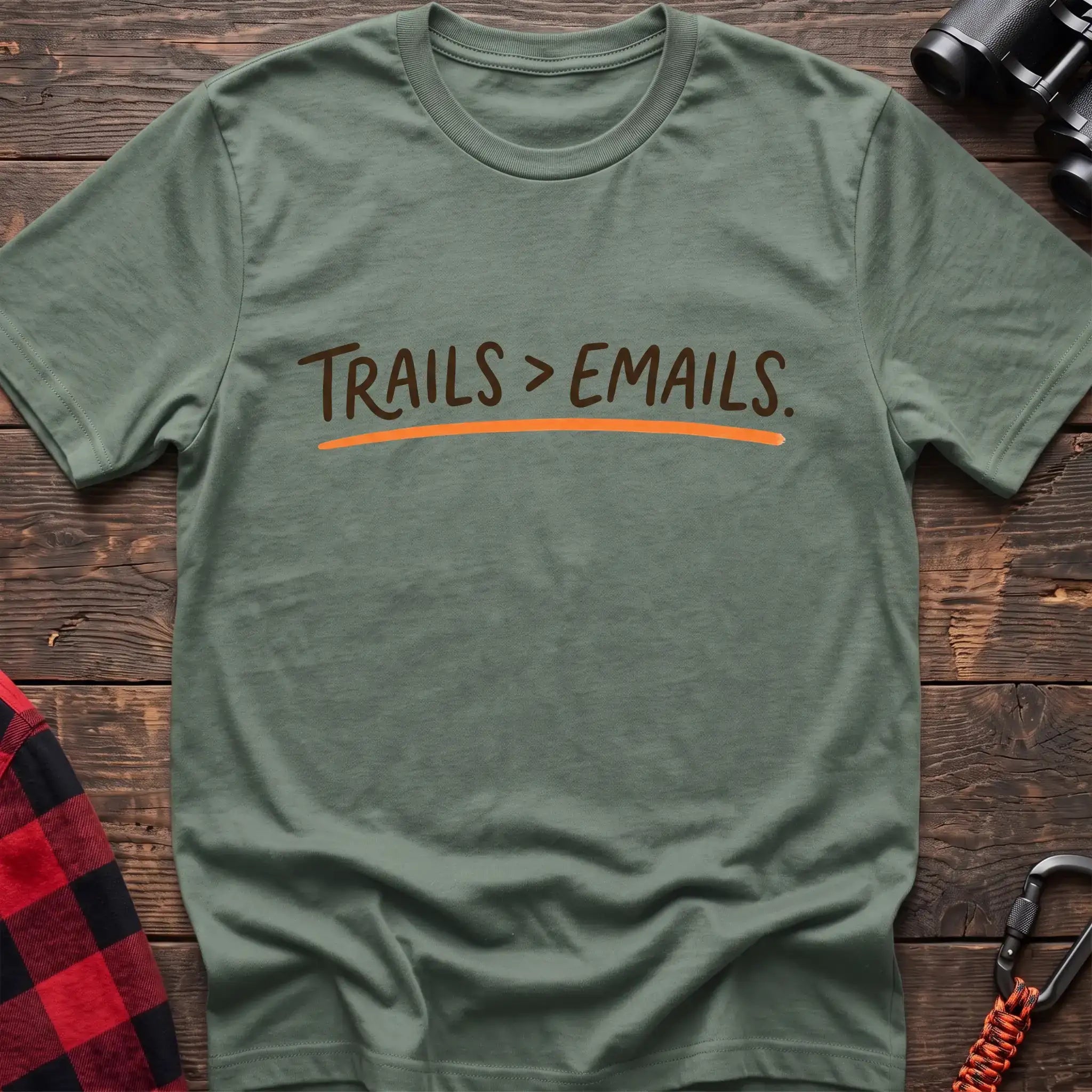 Sage green t-shirt with brown handwritten-style text reading Trails greater than Emails and an orange underline
