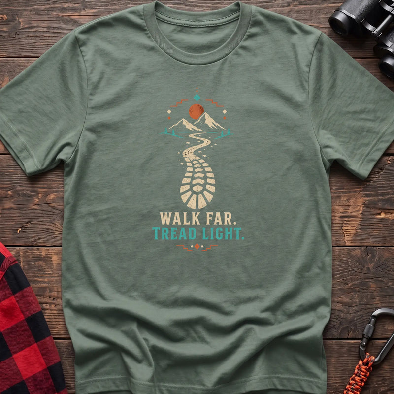 Sage cotton t-shirt with a bootprint trail and mountain graphic and Walk Far Tread Light text on rustic wood