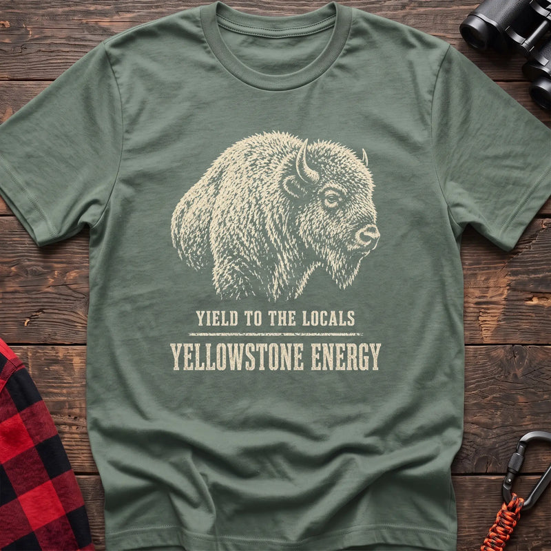 Sage cotton t-shirt with a bison graphic and Yield to the Locals Yellowstone Energy text on rustic wood