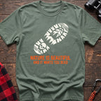 Sage t-shirt with white boot print graphic featuring a skull and pine trees, and orange text reading Nature Is Beautiful And It Wants You Dead