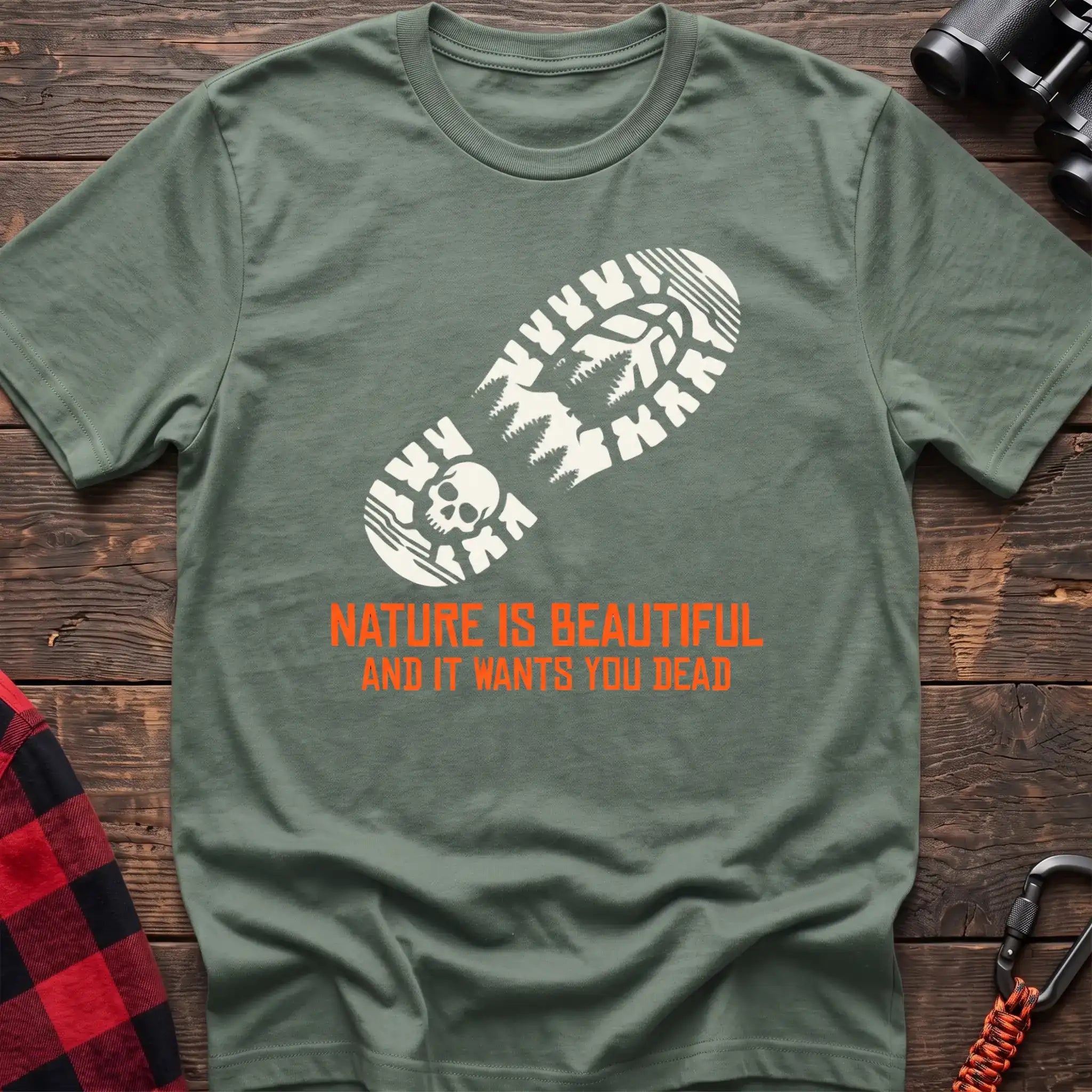 Sage t-shirt with white boot print graphic featuring a skull and pine trees, and orange text reading Nature Is Beautiful And It Wants You Dead