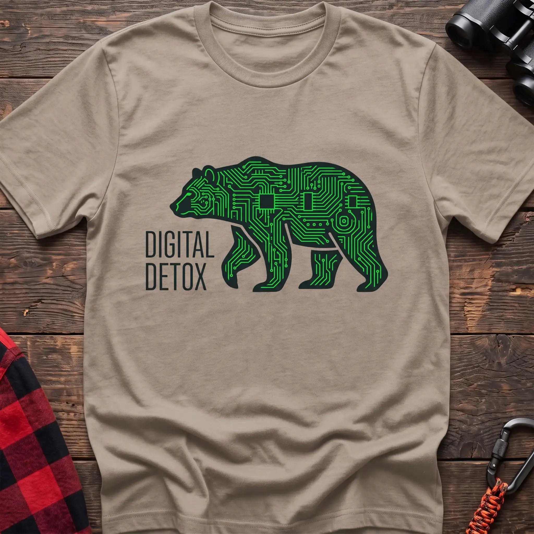 Sand t-shirt with a neon green circuit-board patterned silhouette of a walking bear, and the text “DIGITAL DETOX” printed to the left of the design, laid flat on a wooden surface.