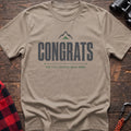 Sand cotton t-shirt with a mountain graphic and Congrats You Still Have to Walk Down text on rustic wood