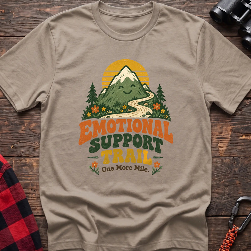 Sand cotton t-shirt with a smiling mountain and trail graphic and Emotional Support Trail text on rustic wood