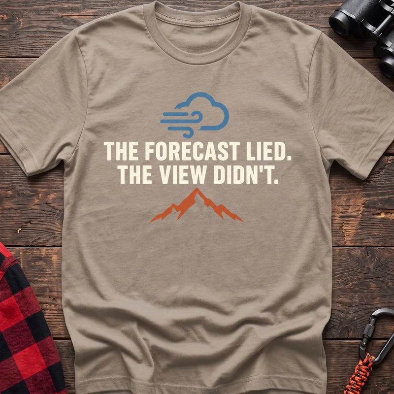 Sand cotton t-shirt with a wind cloud and mountain graphic and The Forecast Lied The View Didn’t text on rustic wood