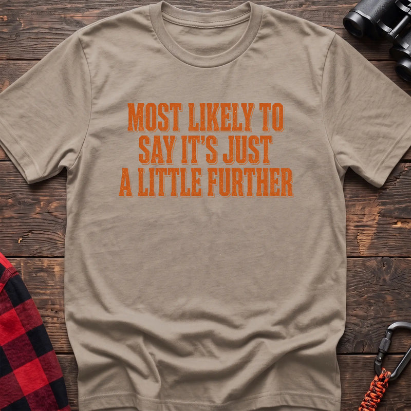 Sand cotton t-shirt with Most Likely to Say It’s Just a Little Further text on rustic wood