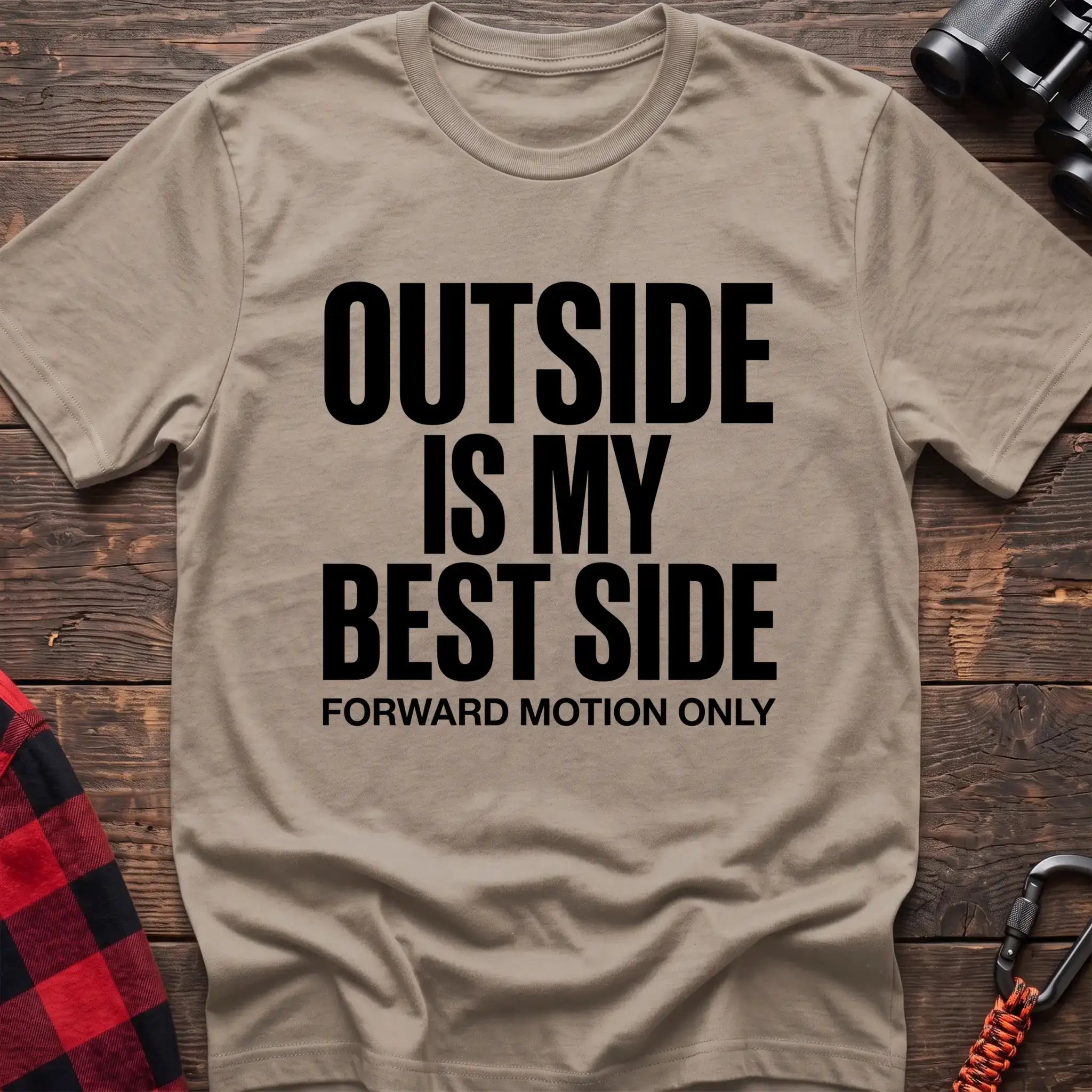 Sand t-shirt with bold black text reading “OUTSIDE IS MY BEST SIDE” and “FORWARD MOTION ONLY” below it, laid flat on a wooden surface.