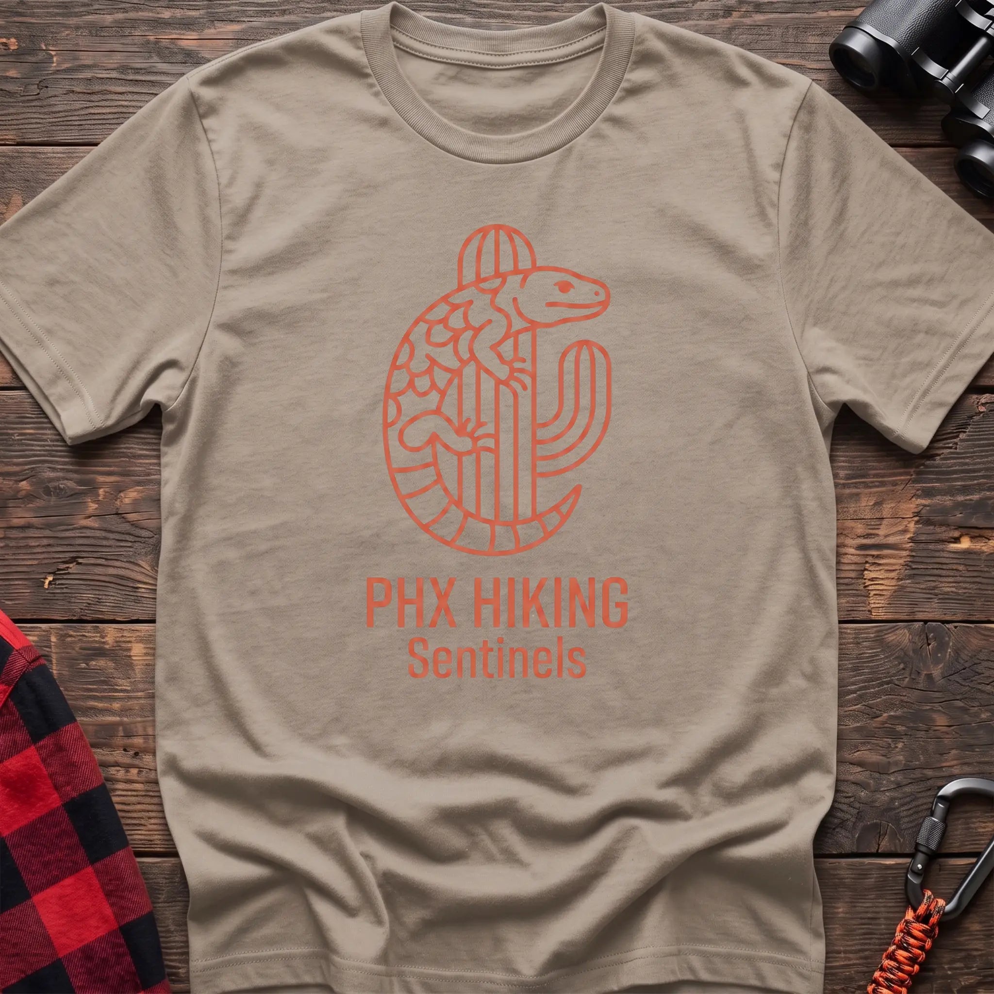 Sand t-shirt with orange line-art Gila monster wrapped around a saguaro cactus and the text “PHX HIKING Sentinels”