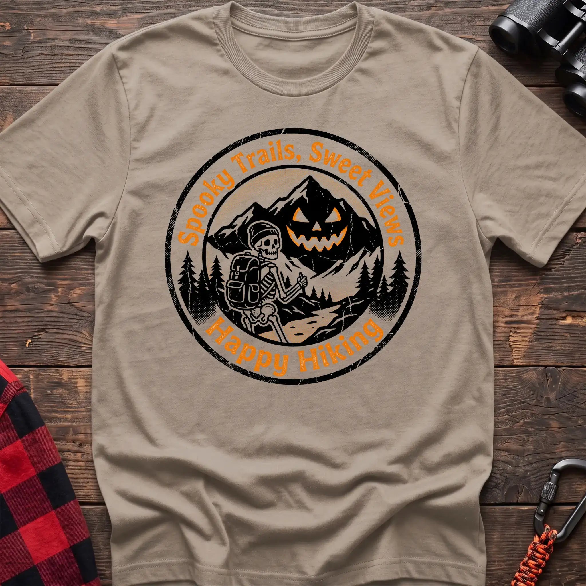 Sand t-shirt with circular graphic of a skeleton hiker giving a thumbs up in front of a jack-o-lantern mountain, reading Spooky Trails Sweet Views Happy Hiking