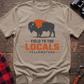 Sand cotton t-shirt with a bison graphic and Yield to the Locals Yellowstone text on rustic wood