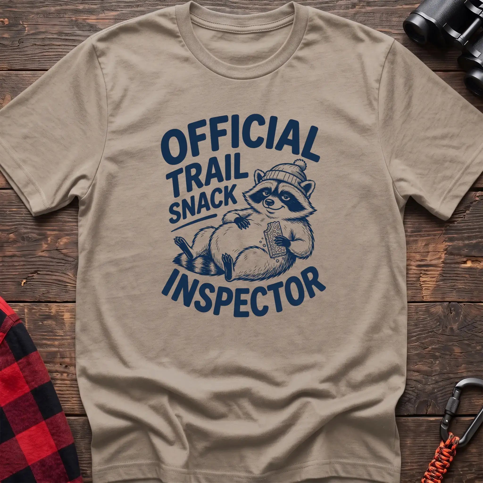 Sand t-shirt with cartoon raccoon holding a snack and the text Official Trail Snack Inspector