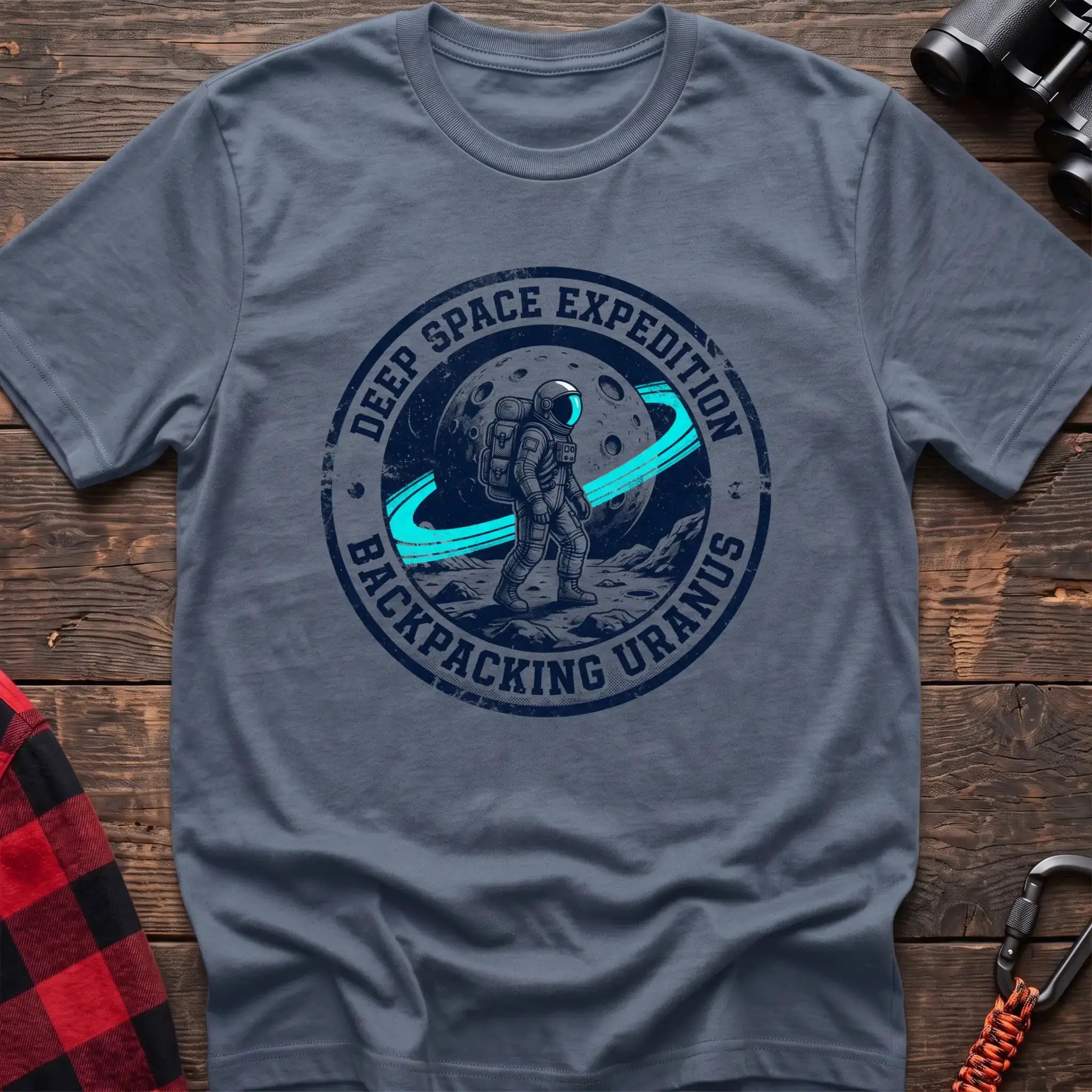 Stone blue t-shirt with circular badge graphic of an astronaut backpacking on Uranus, reading Deep Space Expedition Backpacking Uranus