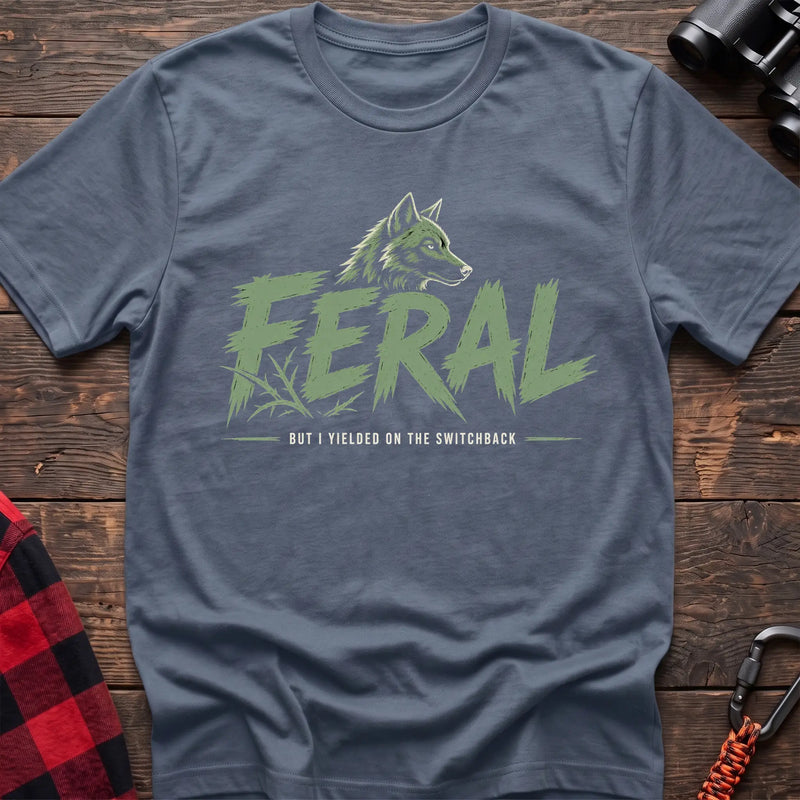Stone bluee cotton t-shirt with a wolf graphic and Feral But I Yielded on the Switchback text on rustic wood