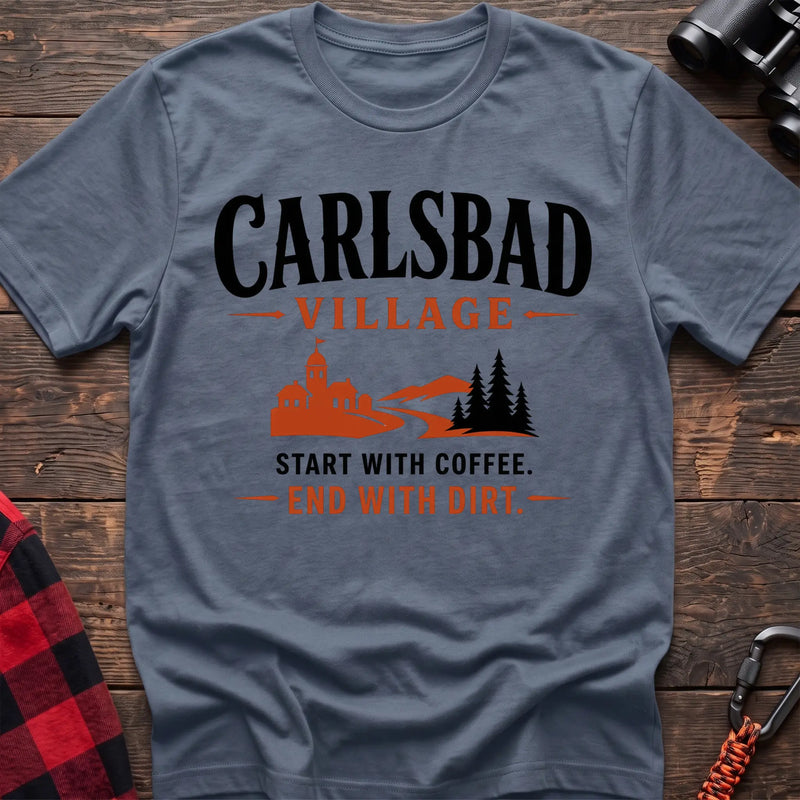 Stone blue cotton t-shirt with a village and trail graphic and Carlsbad Village Start with Coffee End with Dirt text on rustic wood