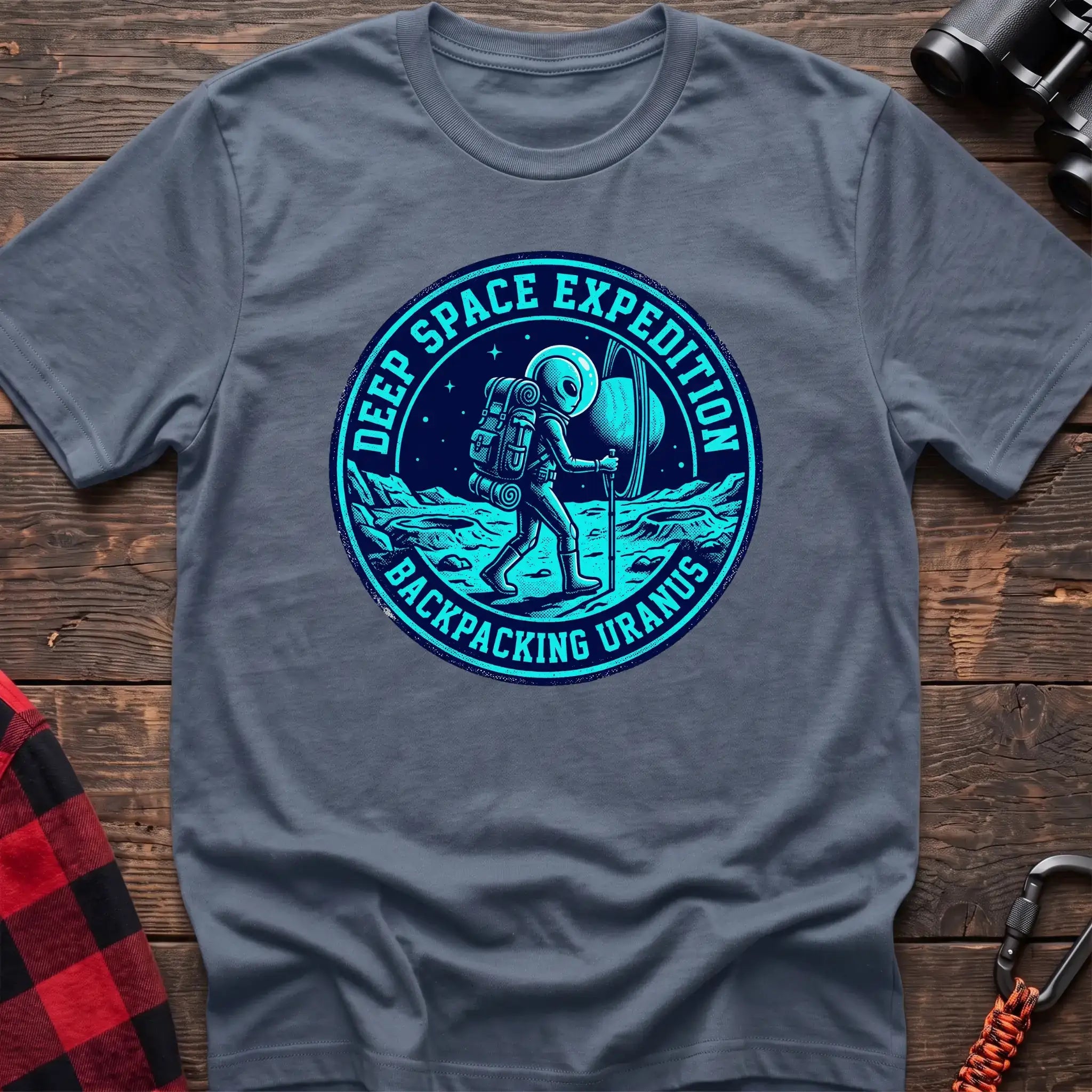 Stone blue t-shirt with circular badge graphic of an alien backpacking on Uranus, reading Deep Space Expedition Backpacking Uranus