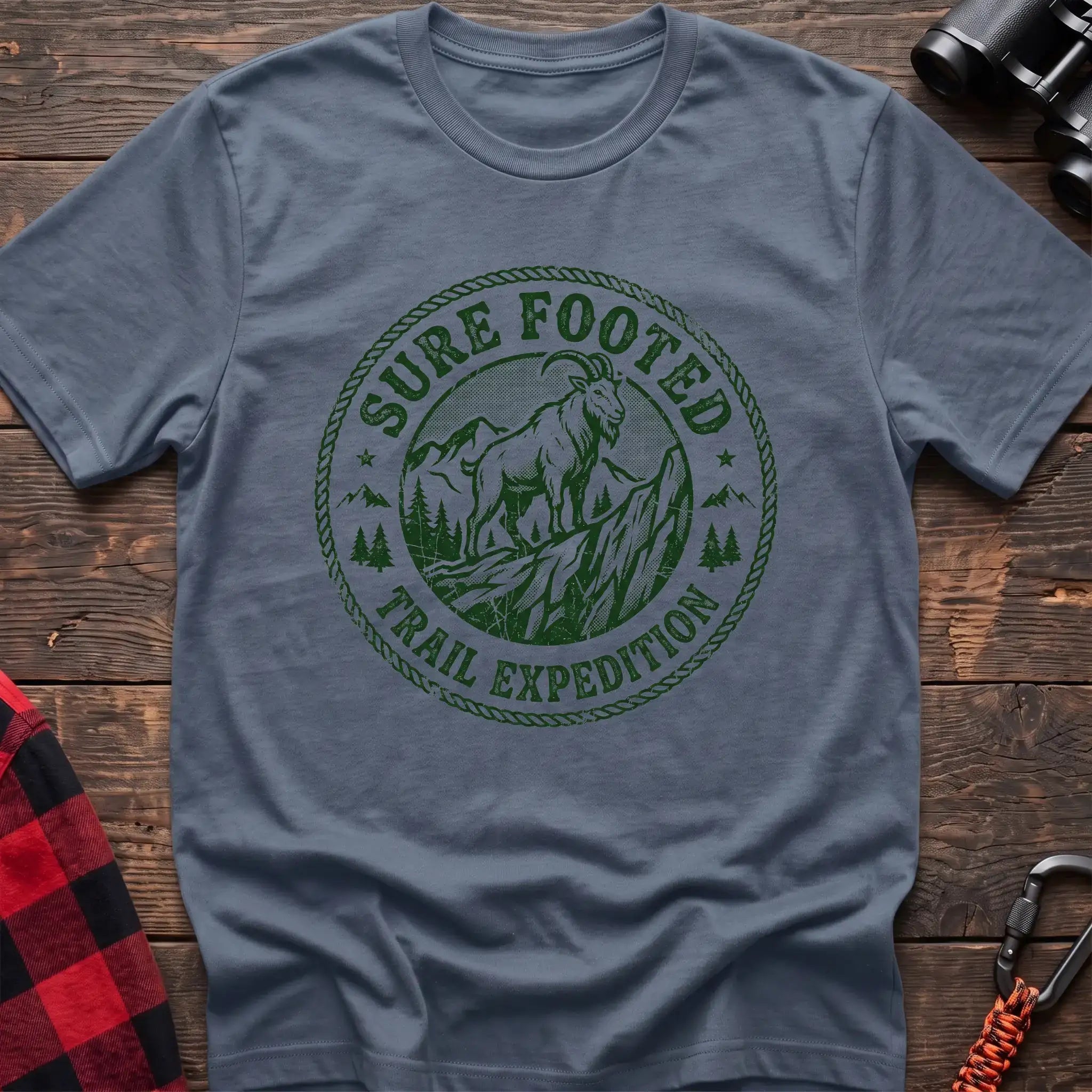 Stone blue t-shirt with circular badge graphic of a mountain goat on a rocky peak reading Sure Footed Trail Expedition