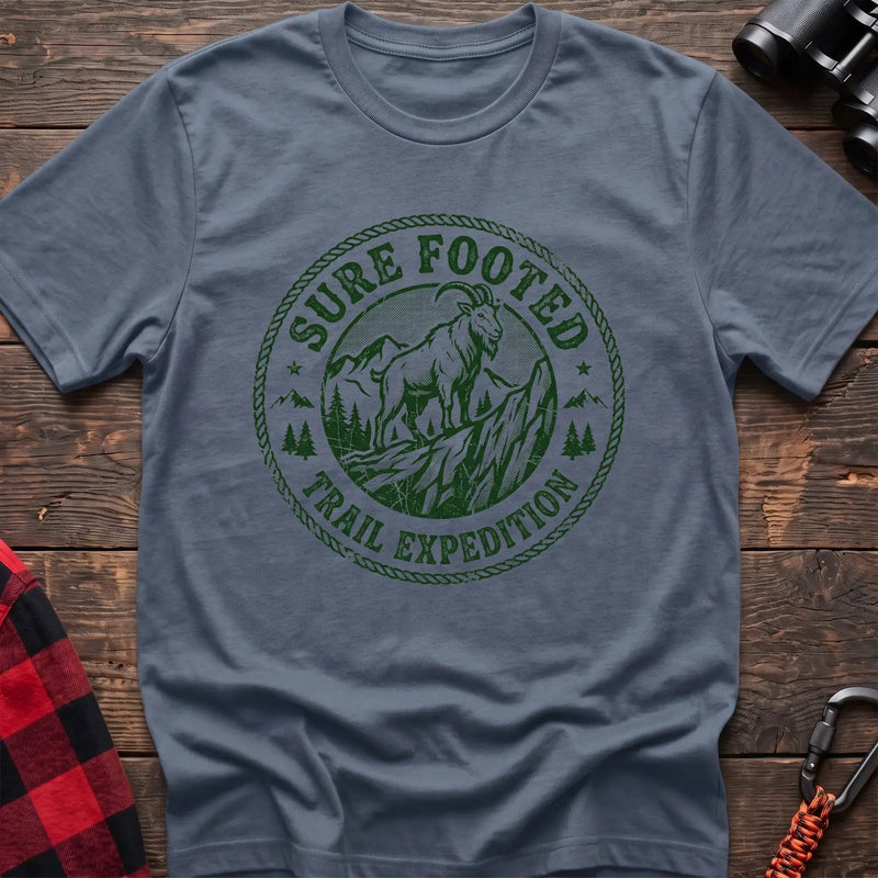 Stone blue t-shirt with circular badge graphic of a mountain goat on a rocky peak reading Sure Footed Trail Expedition