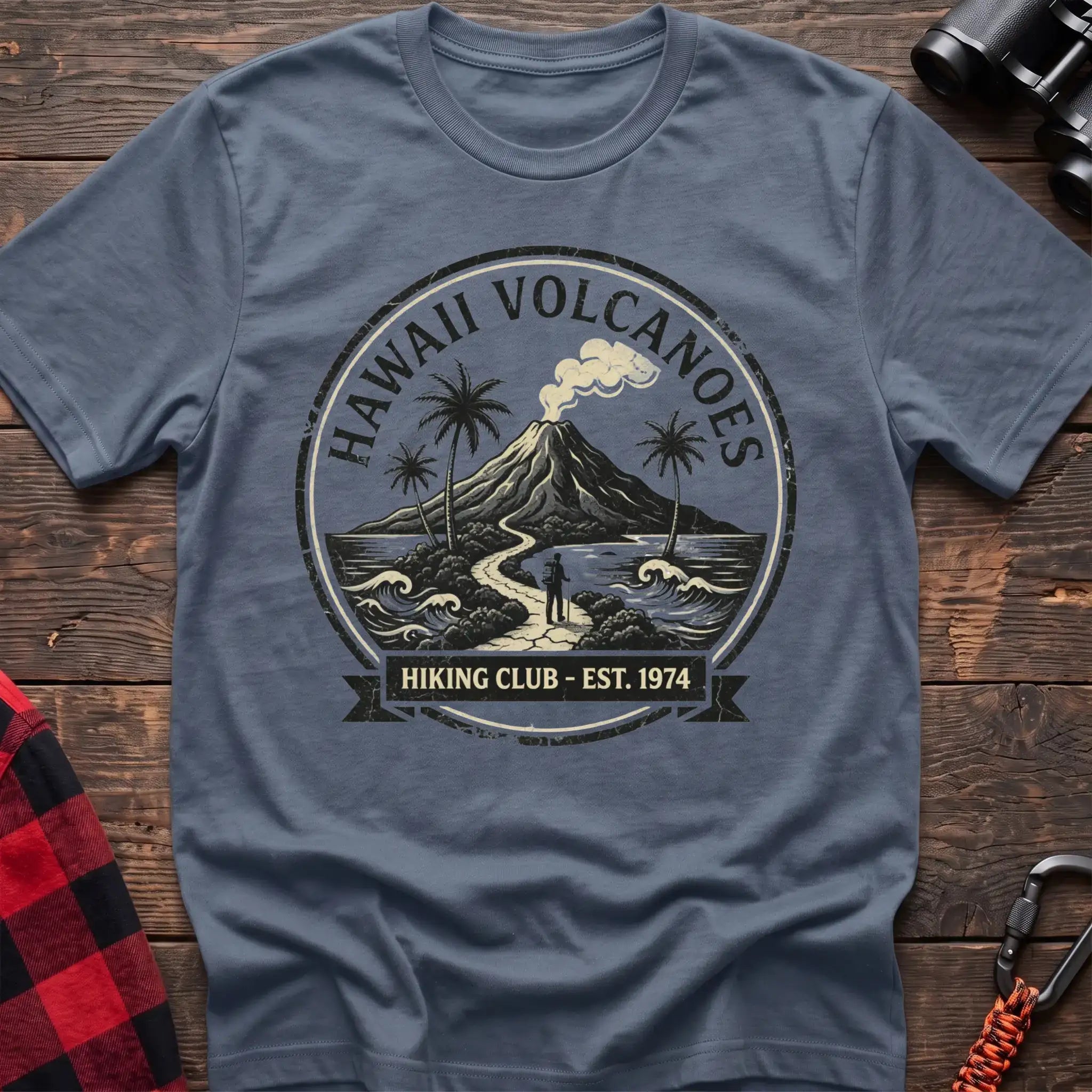 Stone blue t-shirt with circular Hawaii Volcanoes badge graphic showing a volcano, palm trees, and a hiker, reading Hiking Club Est 1974