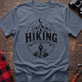 Stone blue cotton t-shirt with vintage Hiking for Adventure graphic of mountains under a crescent moon and a hiker on a trail, flat lay on rustic wood with hiking gear