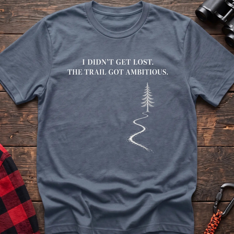 Stone blue cotton t-shirt with a winding trail graphic and I Didn’t Get Lost The Trail Got Ambitious text on rustic wood